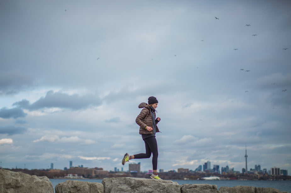 Person running alongside water with a cityscape and grey clouds in the background 