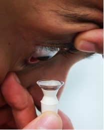 Person looking down and inserting a contact lens with a device