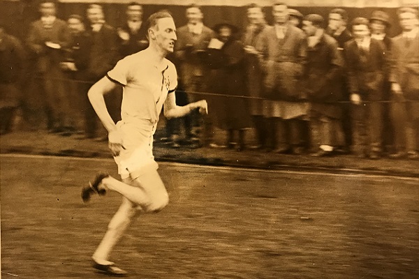 Sepia image of Moorfields athlete Stallard running in front of a crowd