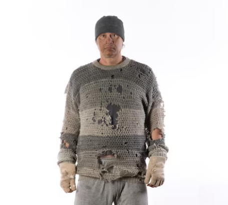 Person with a dirty face wearing a dirty jumper with lots of holes in it