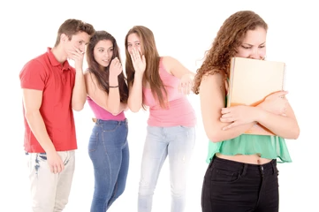 Three people whispering together behind the back of a person holding a folder close to their chest and looking down