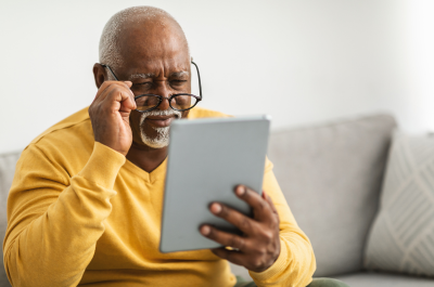 A mature man holding his glasses and looking at his laptop