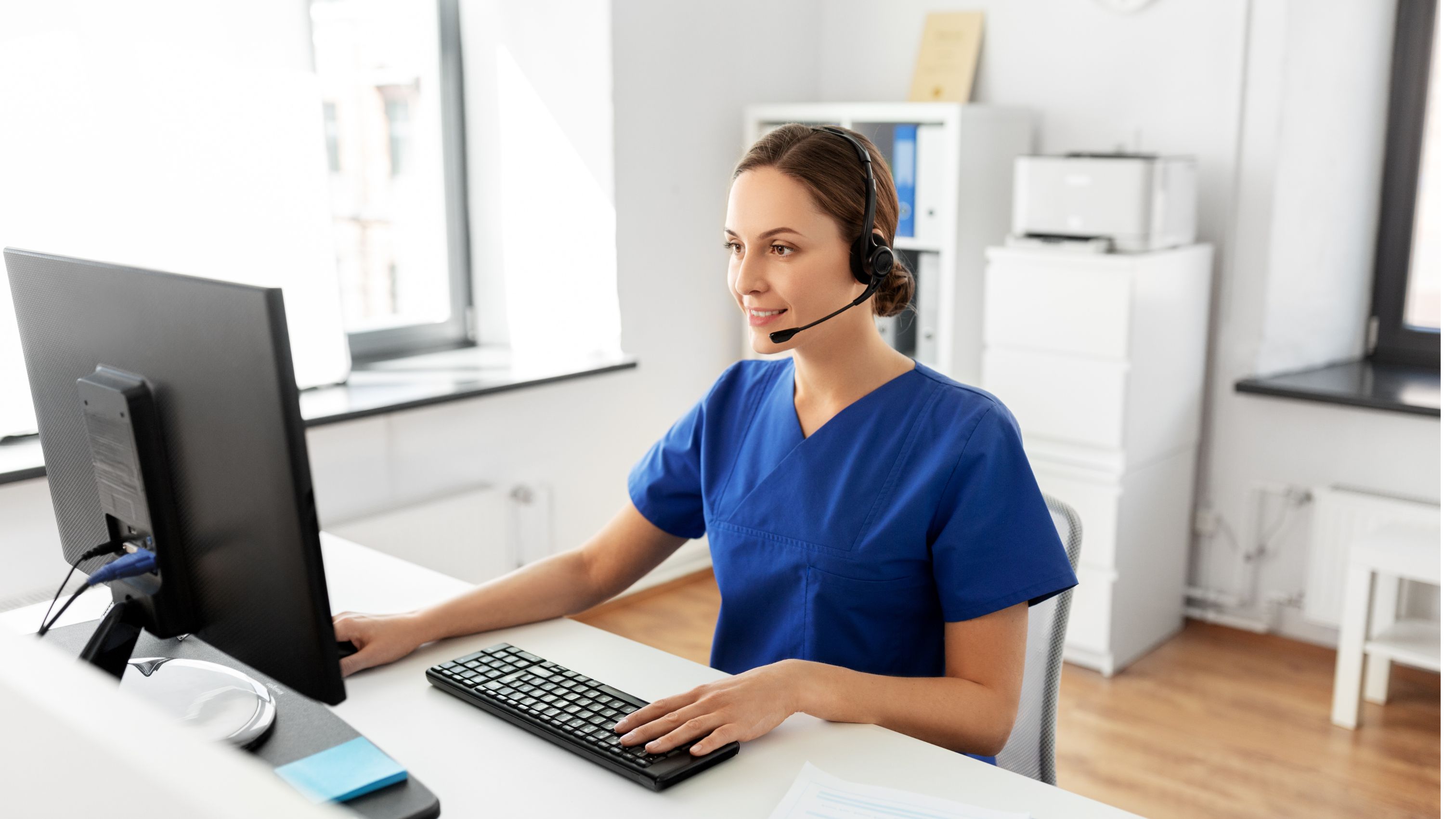 Person sitting at a desk looking at a computer in a predominately white room