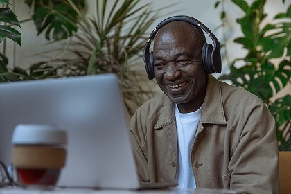 A senior man in headphones looking at his laptop screen and smiling