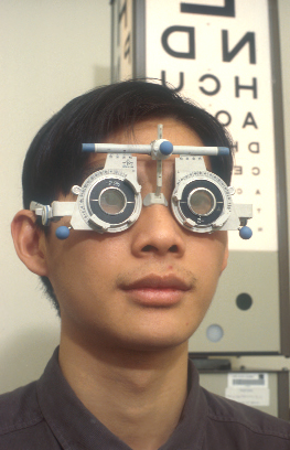 Patient wearing eye examination glasses with an eye chart 